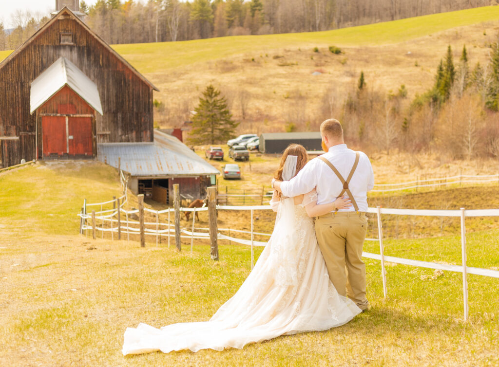 The bride and groom look across the field at their farmlands as they anticipate this new chapter in their life in the mountains of Vermont.