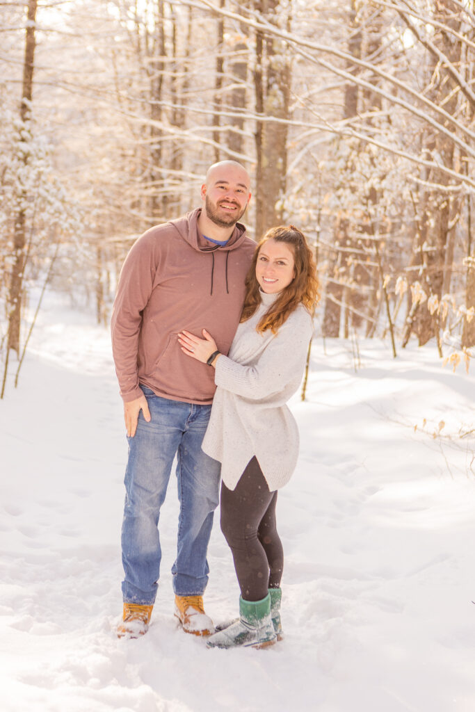 Brendan and Mia stand together on a snowy hiking trail in the Lakes Region.