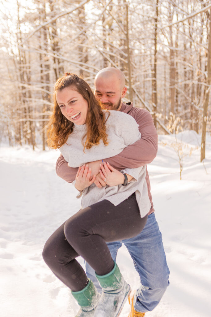 Brendan runs up behind Mia to pick her up, making her laugh during their snowy engagement session in NH.