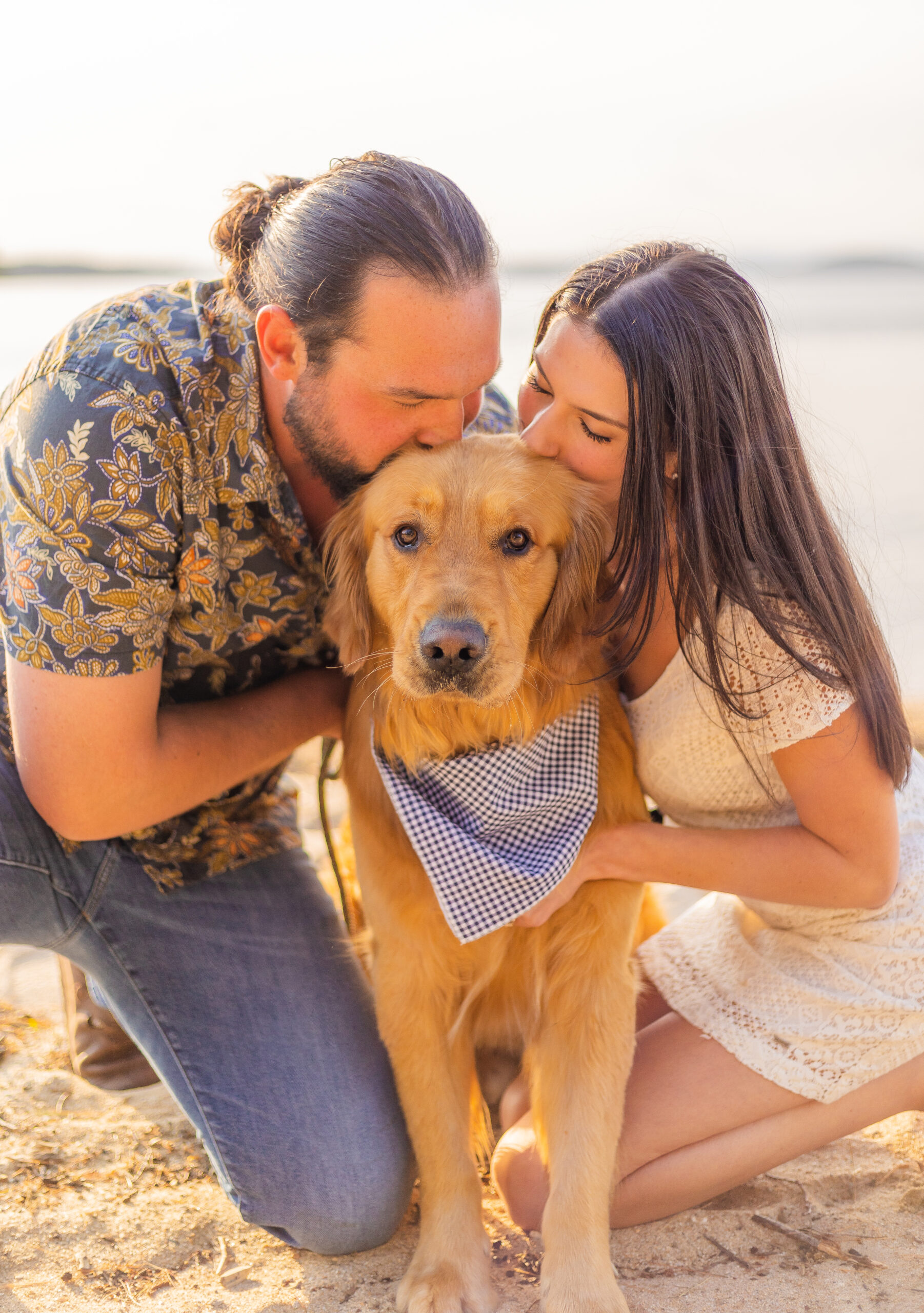 An engaged couple kissing their golden retriever on the head at Ellacoya State Park.