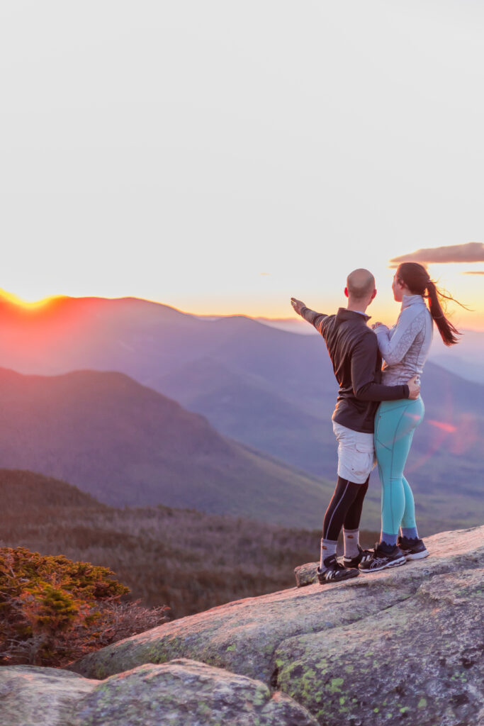 The future bride and groom admire the sunrise in the mountains on top a 4000 footer in NH.  
