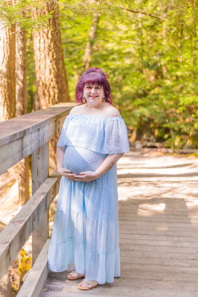 Rose holds her pregnant belly on a bridge on a river at The Basin in NH.