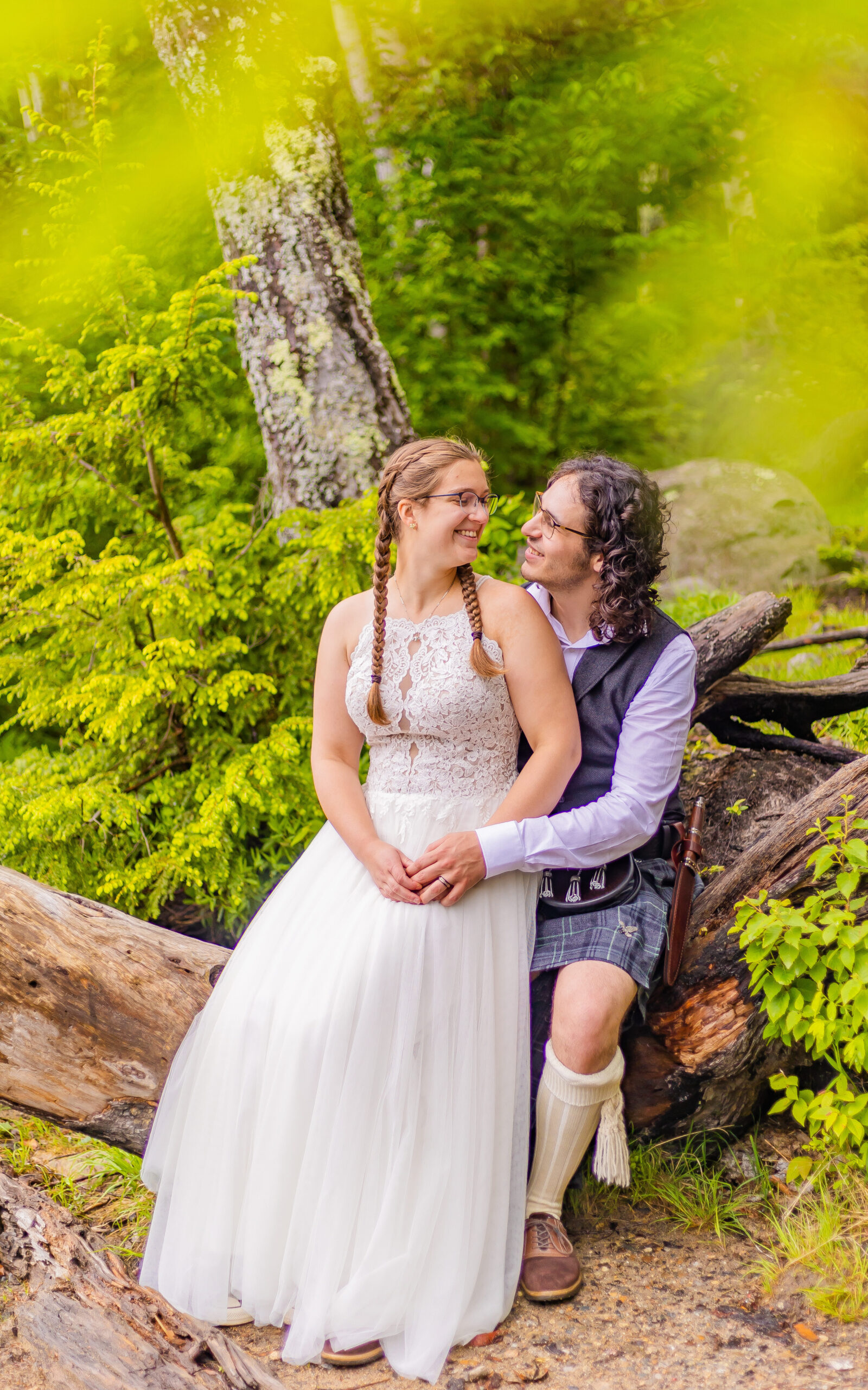 The bride and groom sit together on a log staring into each other's eyes.
