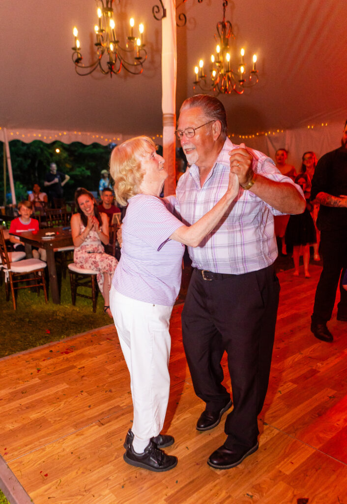 Two grandparents hold hands and dance together during the anniversary dance at a wedding in NH.