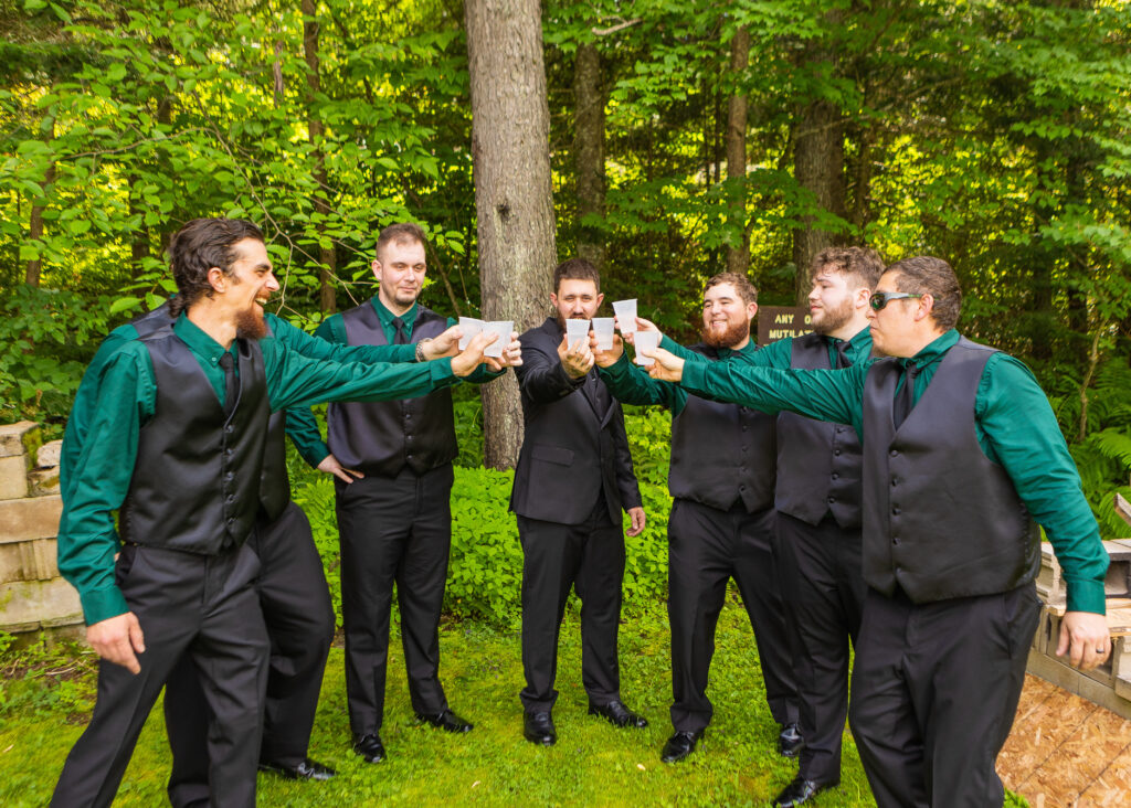 The groomsmen take shots together before the ceremony and clink glasses at their outdoor wedding venue in NH. 
