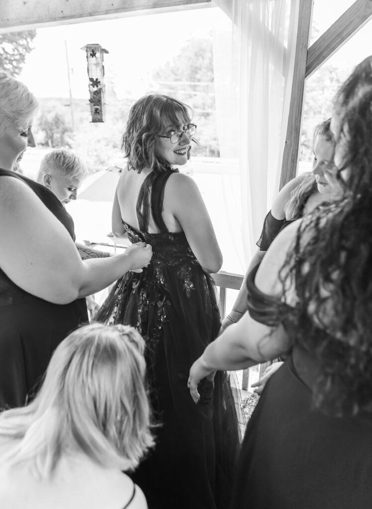 Bride looks over her shoulder while her bridesmaids help her get her dress on in the White Mountains.