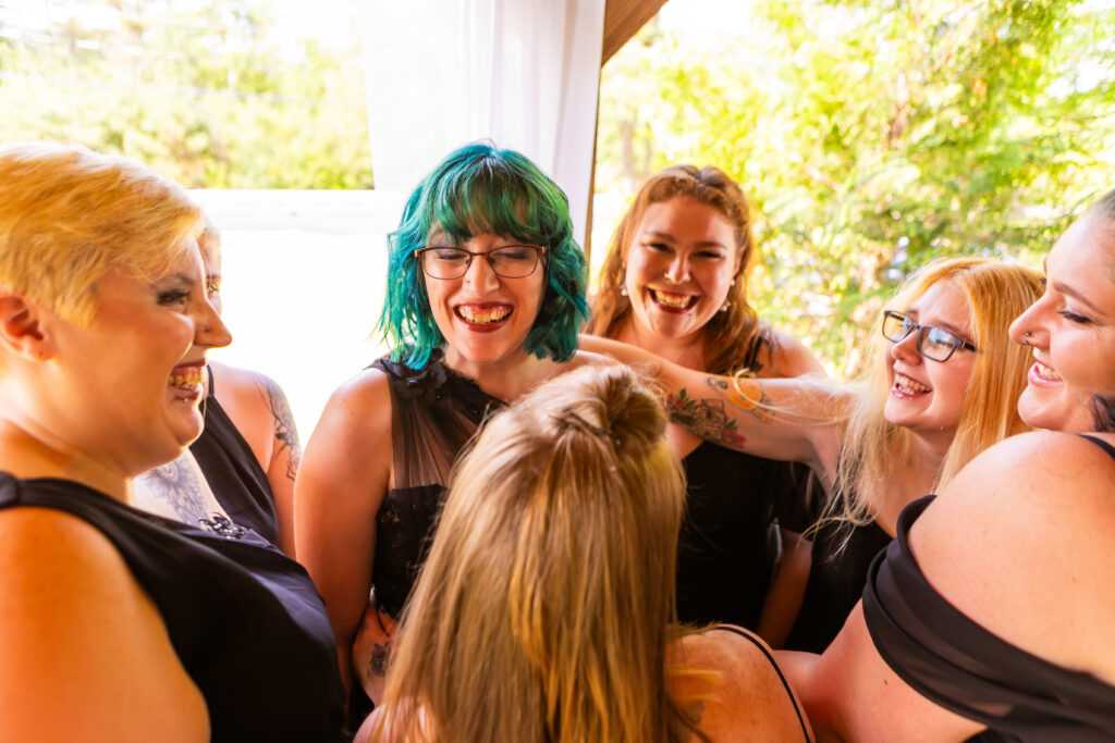The bride and her bridesmaids laugh together while going in for a hug at their small wedding venue in NH.