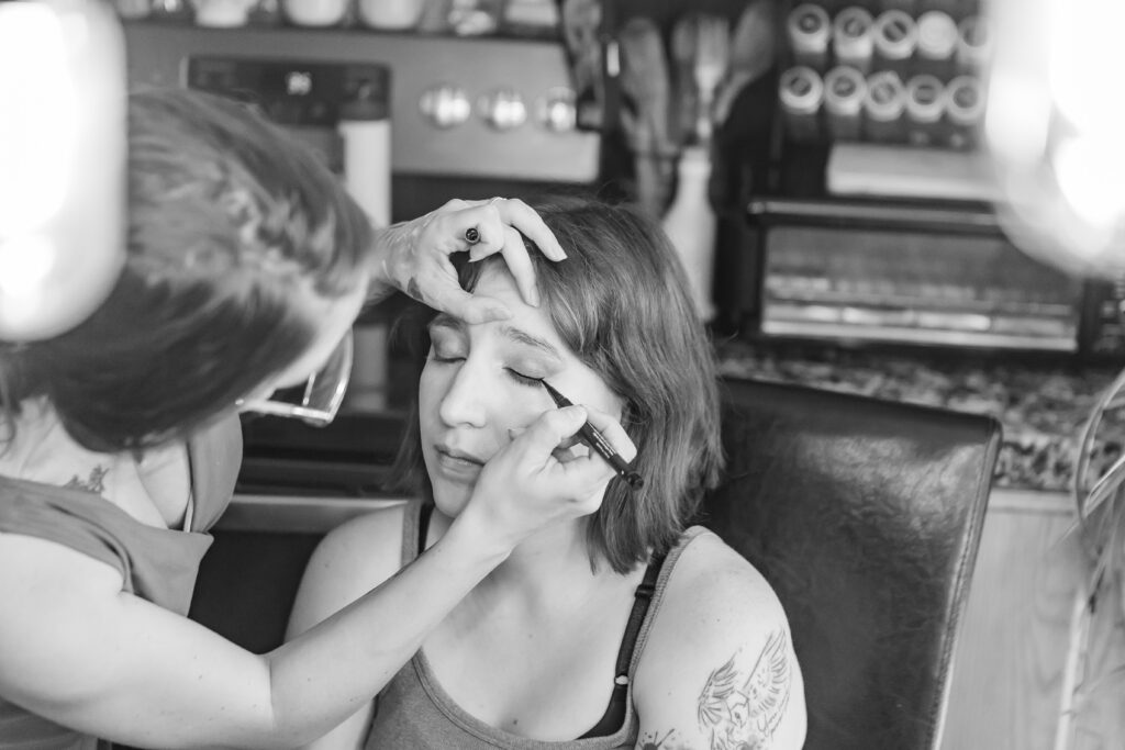 The bride is getting her makeup done under the bright lights at her rustic wedding in NH.