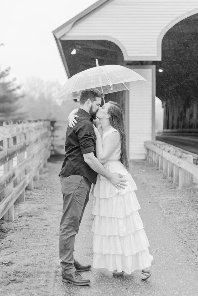 Katie and Ben kiss under their umbrella at an engagement location in NH.