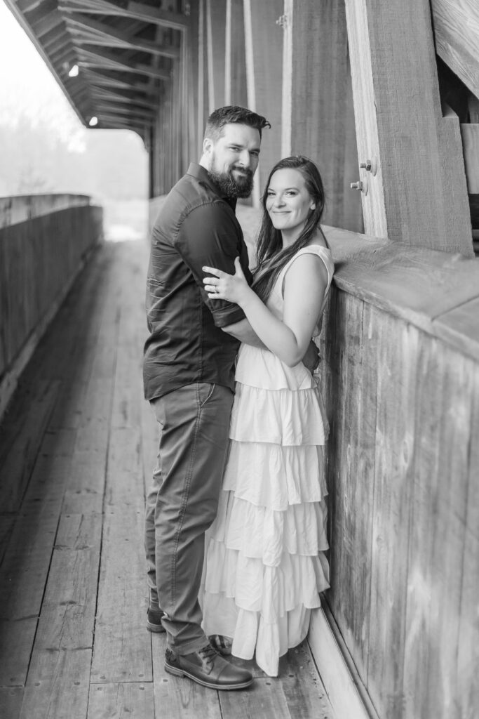 A couple stands under a covered bridge together at an outdoor photo location in New Hampshire.