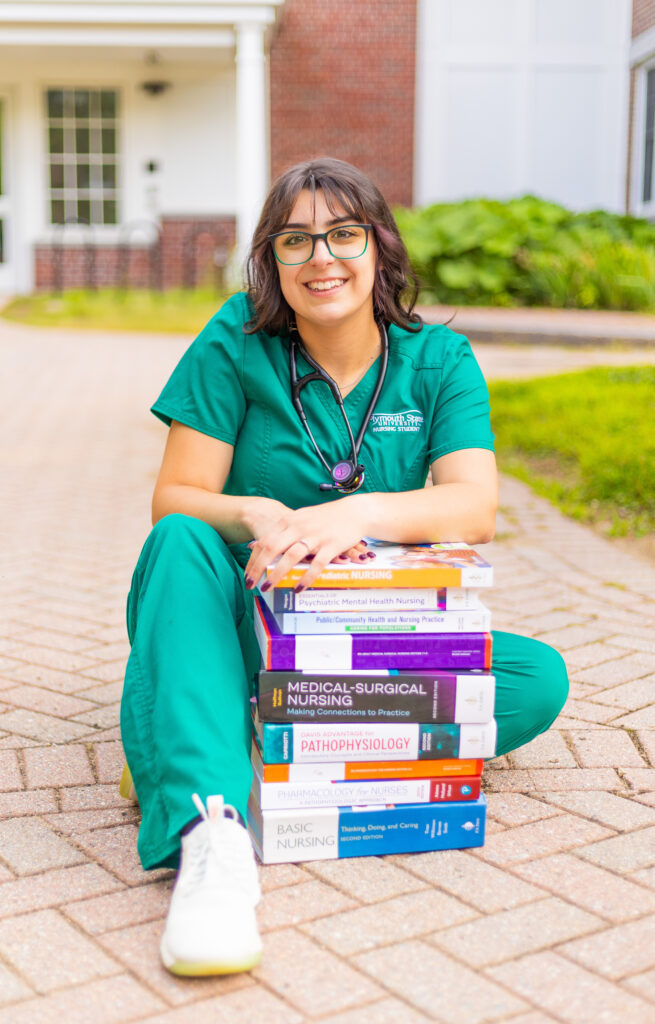 A nursing student poses with her books in from of Samuel Read Hall at Plymouth State University in the White Mountains of Plymouth New Hampshire.