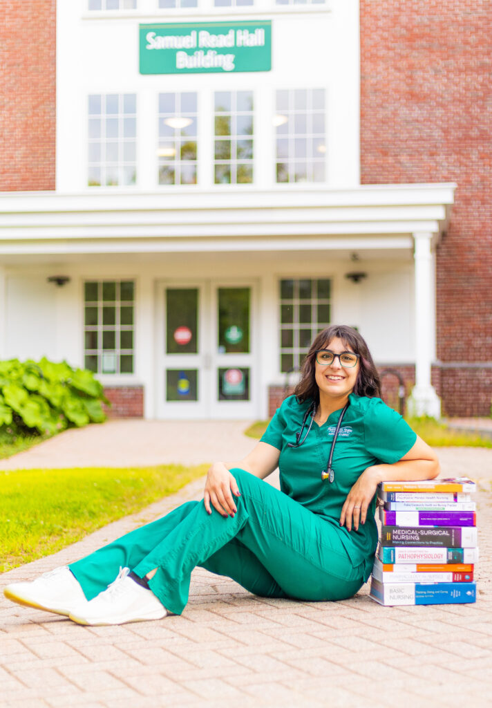 A nursing student sits proudly against her stack of books in Plymouth NH.