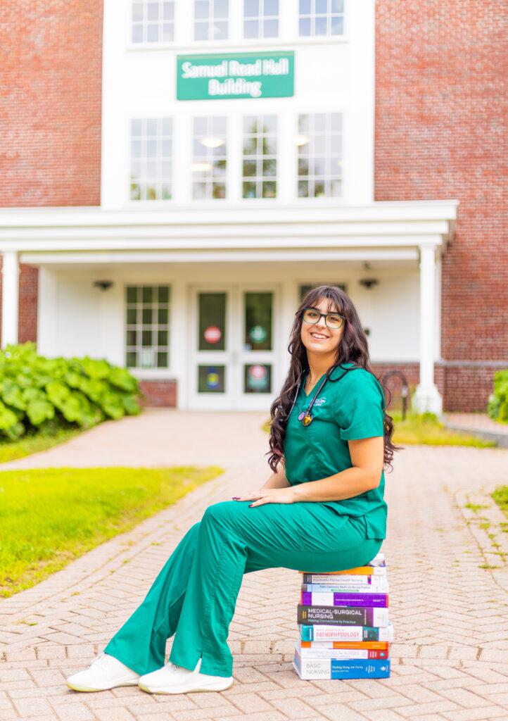 Plymouth State University nursing student sits on top of her books.