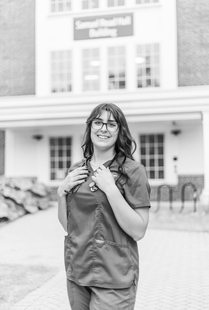 A senior in the Plymouth State University nursing program stands in front of Samuel Read Hall Building.