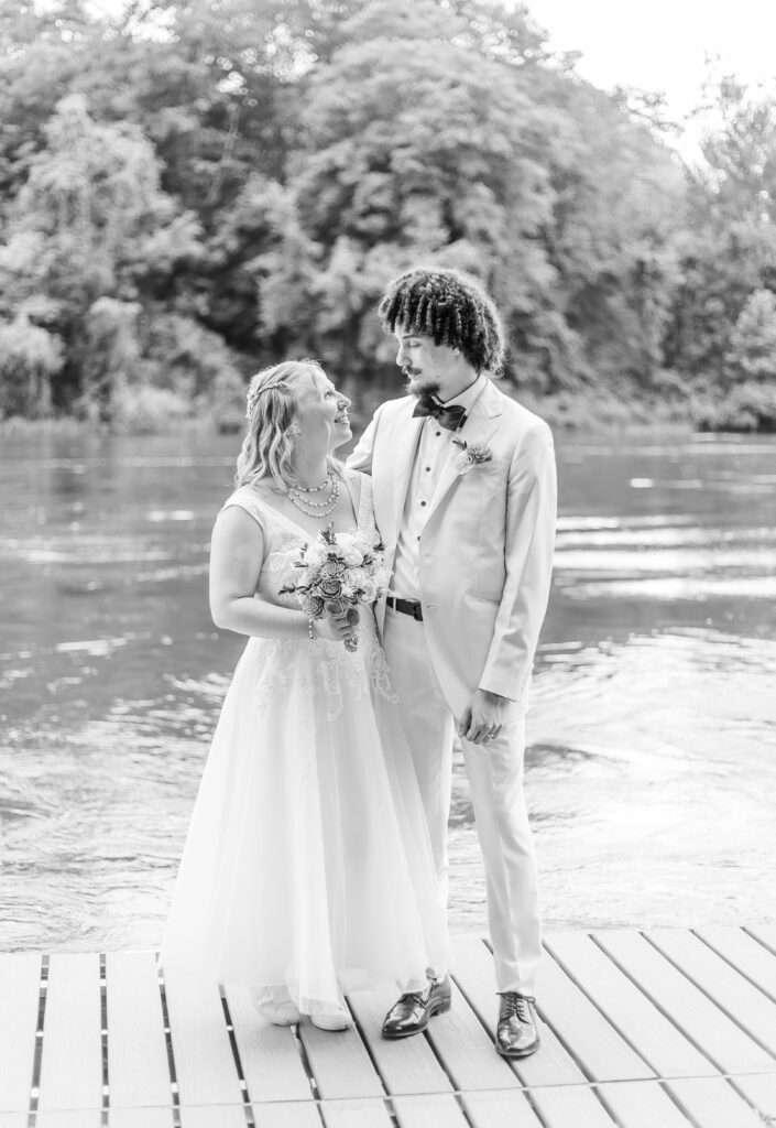 The bride and groom standing on the dock together in front of a river in NH.