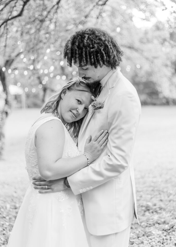Groom holds his bride close under willow trees.