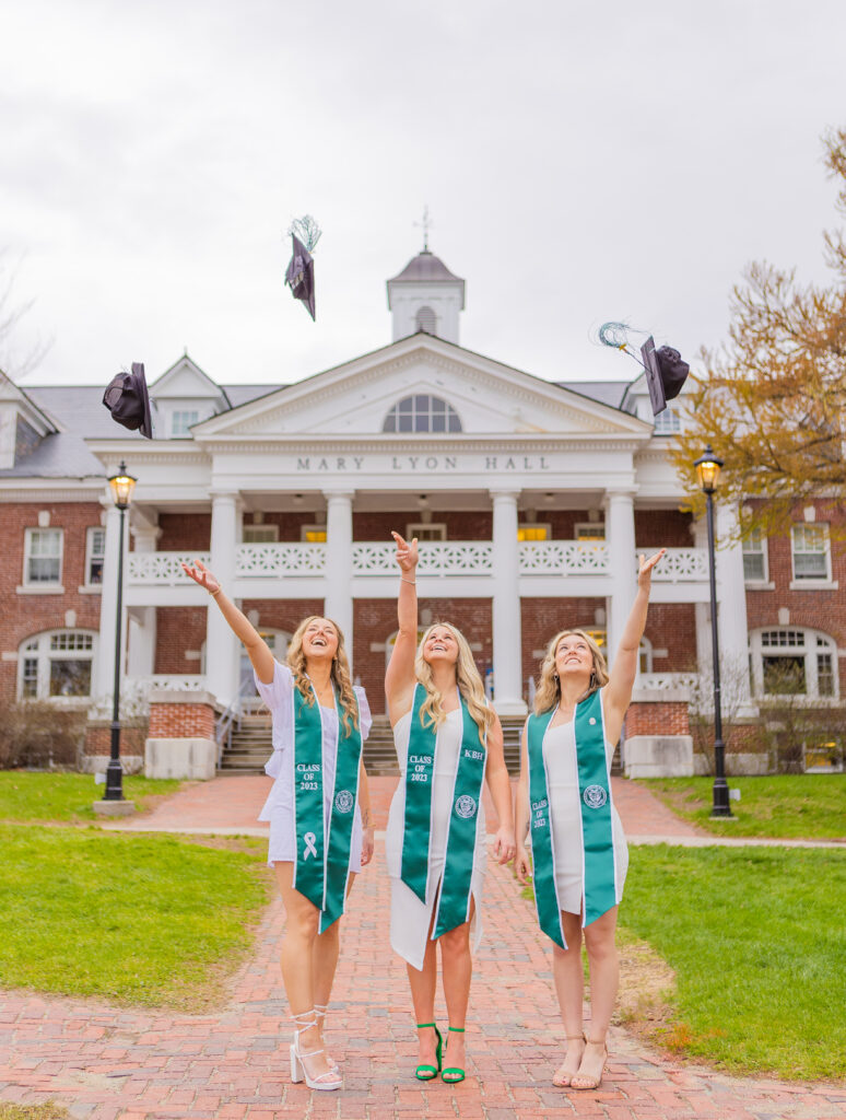 college graduates throwing their cap in front of mary lyon hall at plymouth state university.