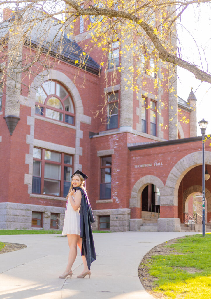 a UNH college grad stands in the golden hour light in front of Thompson Hall in Durham NH.