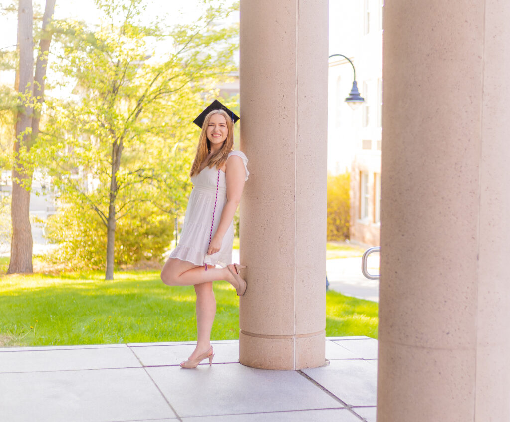 A college at Graduation Photo Sessions at Plymouth State University and UNH leans against a library pillar.