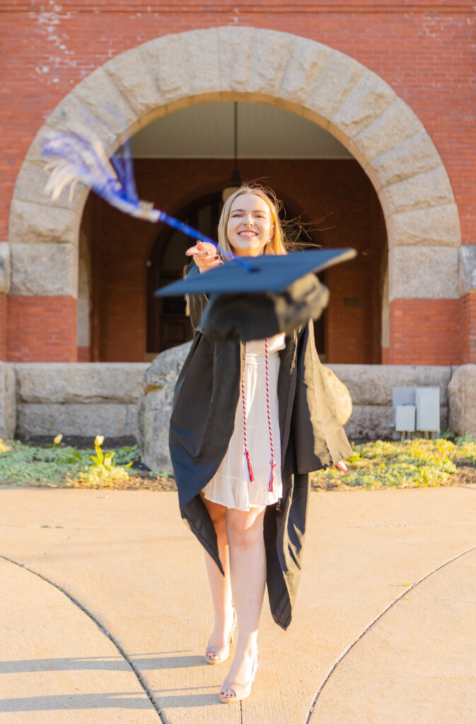 College grad throwing their grad cap in front of Thompson Hall on University of New Hampshire campus.