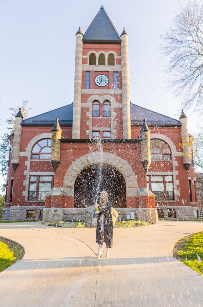 A college grad sprays champagne in front of Thompson Hall at UNH.