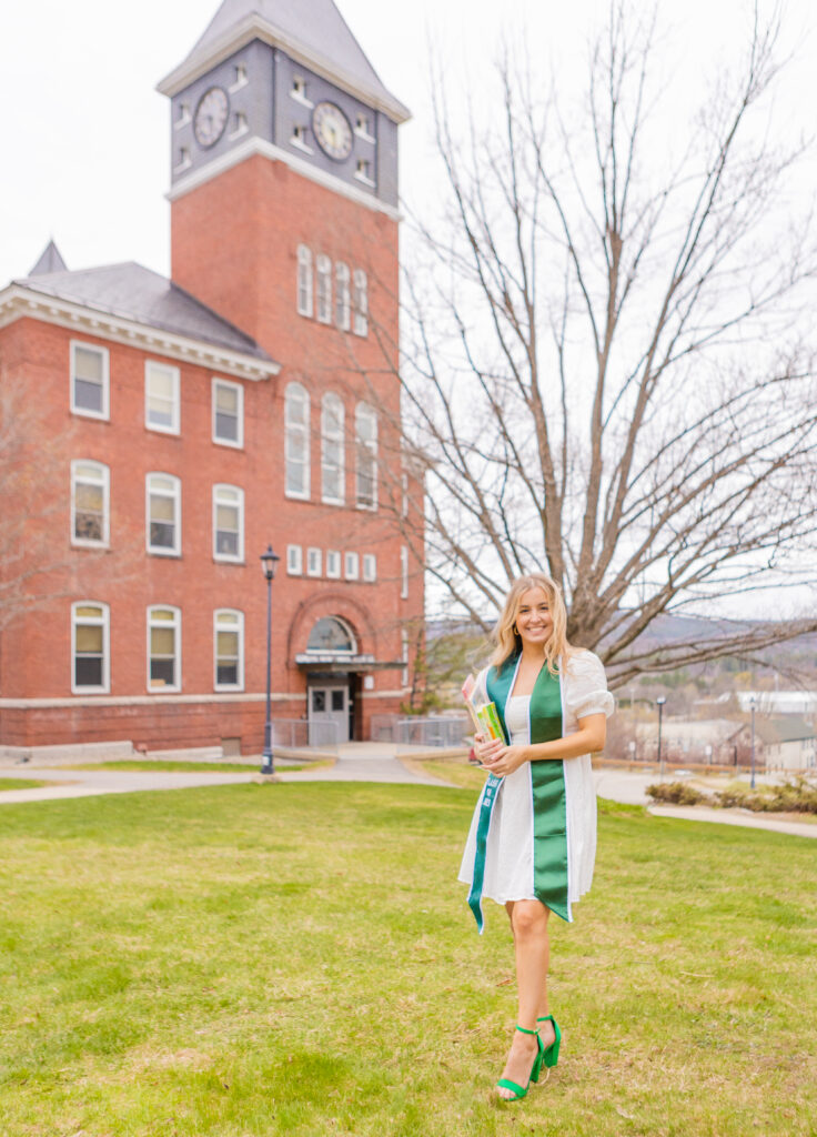 An elementary education college grad stands in front of Rounds Hall in Plymouth, NH.