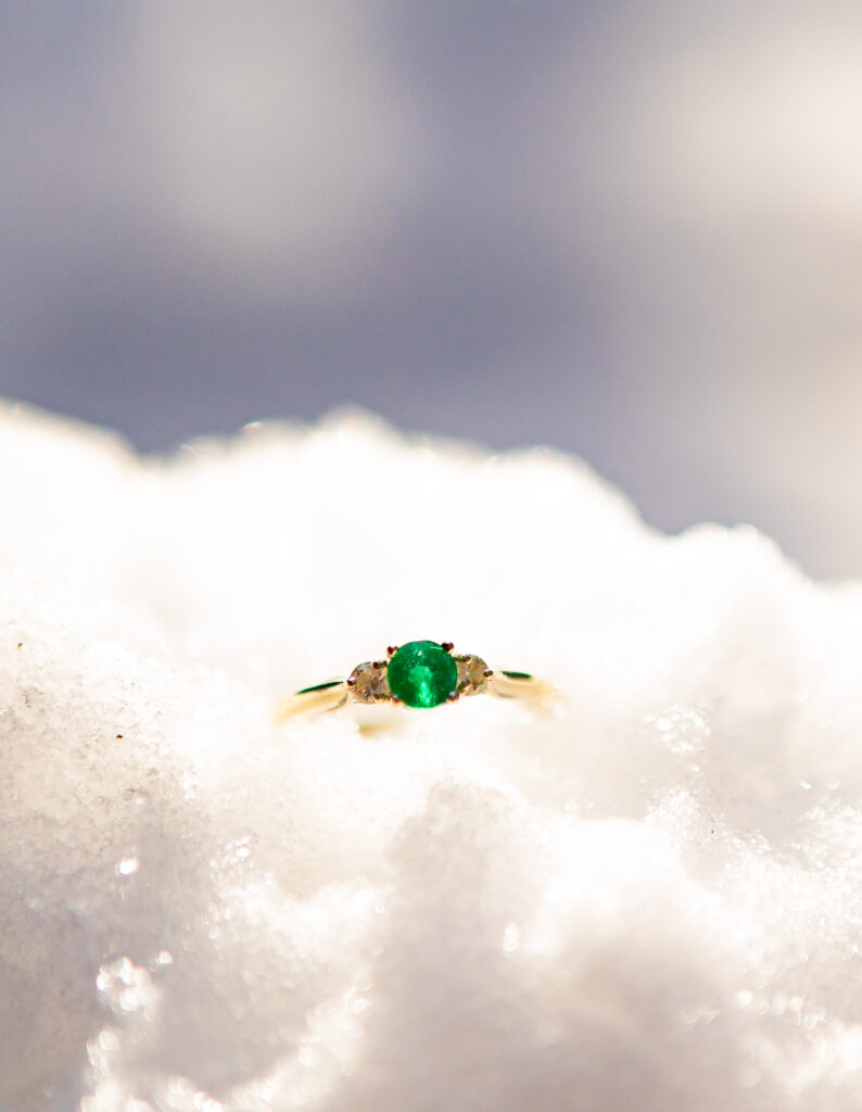 A emerald engagement ring in the snow at an engagment session in Holderness NH.