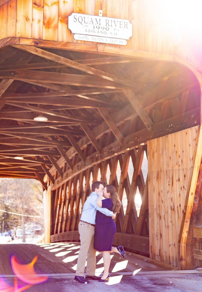 An engaged couples kissed one another at the Squam River Covered Bridge in Ashland NH. 
