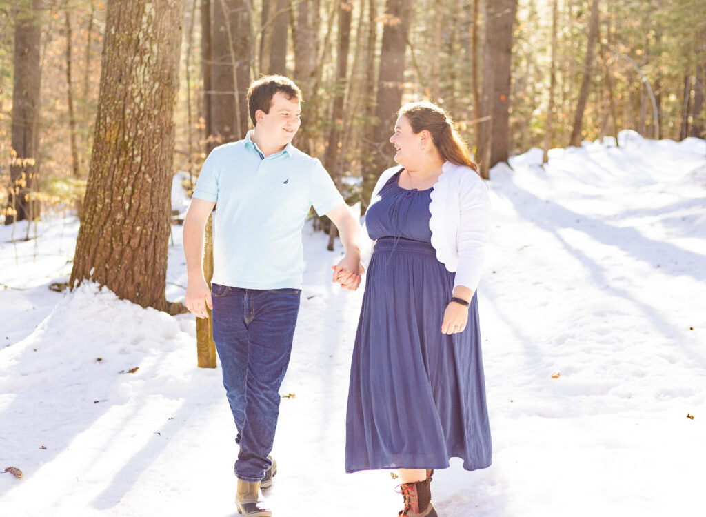 A couple walks holding hands at their woodsy engagement session in the White Mountains.
