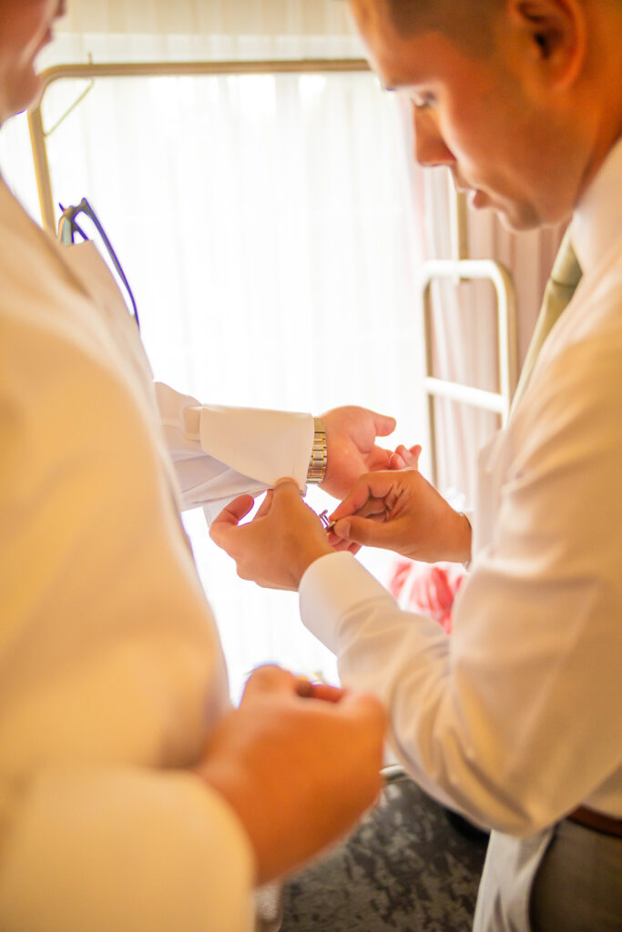 Groomsmen helps the groom with his cufflinks.