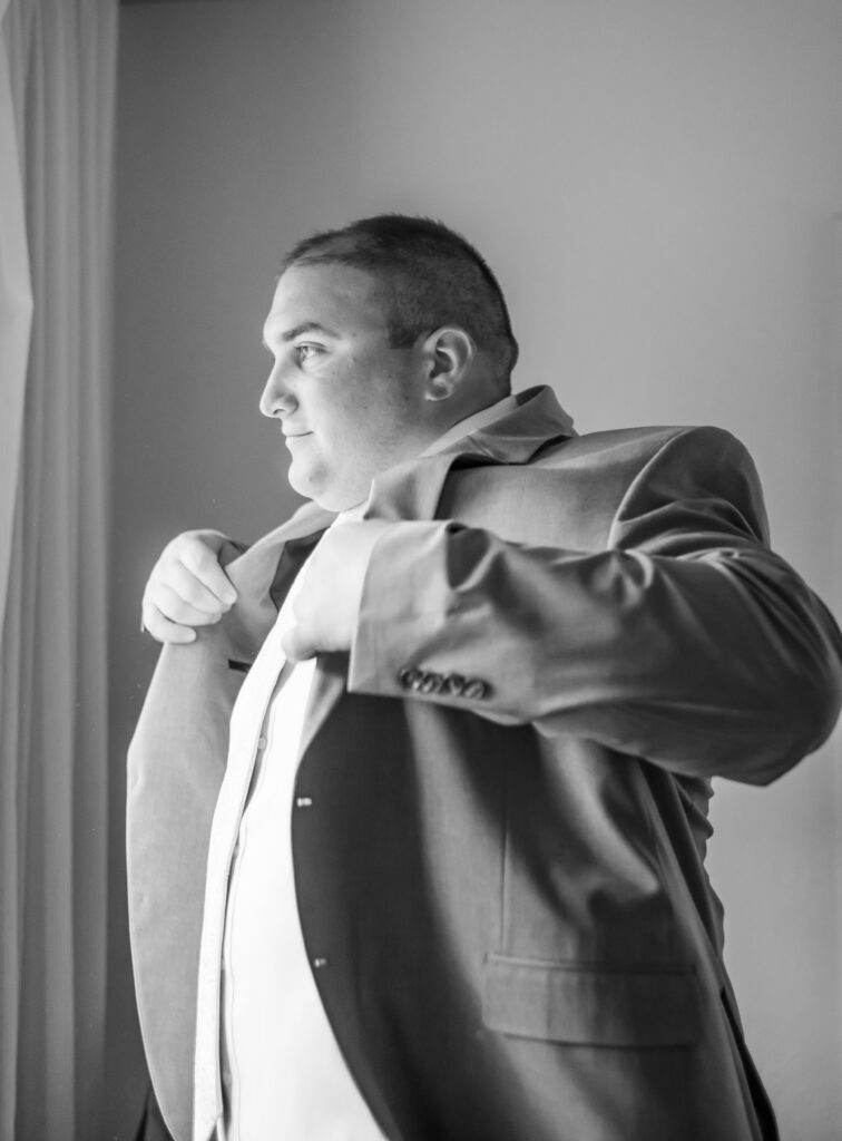 Groom looks out the window thinking about his beautiful bride as he finishes getting ready for his wedding in New Hampshire.