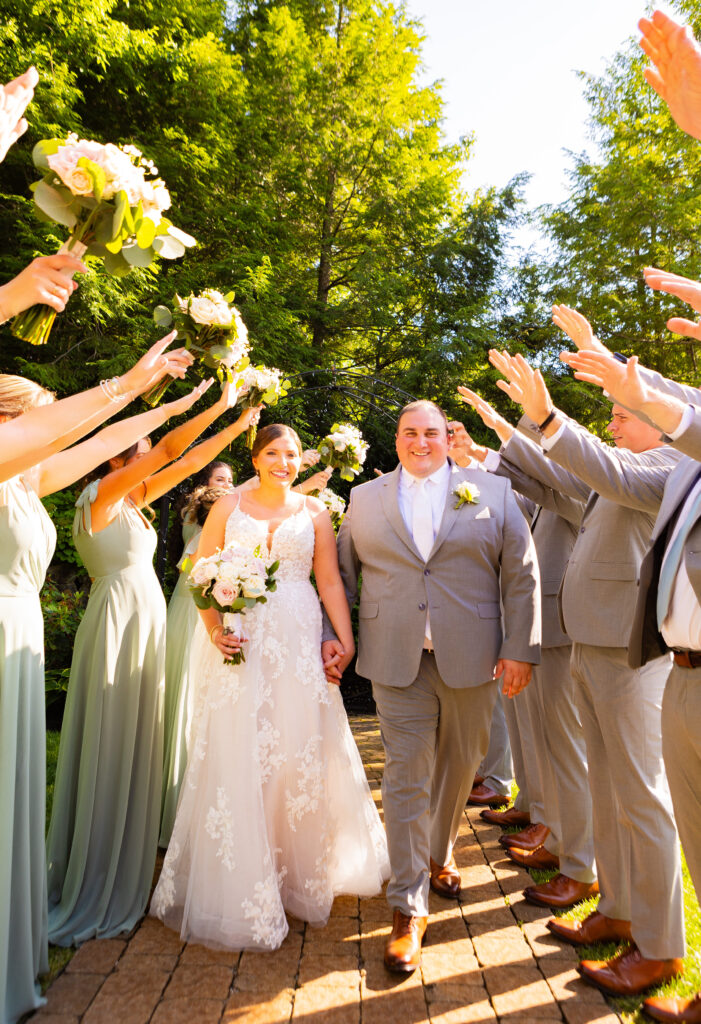 Bride and groom walk under the flowers and hands of their wedding party.