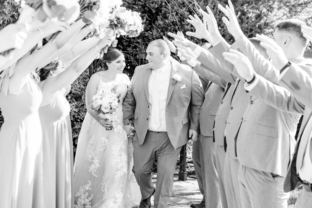 Bride and groom walk through a tower made by their wedding party.