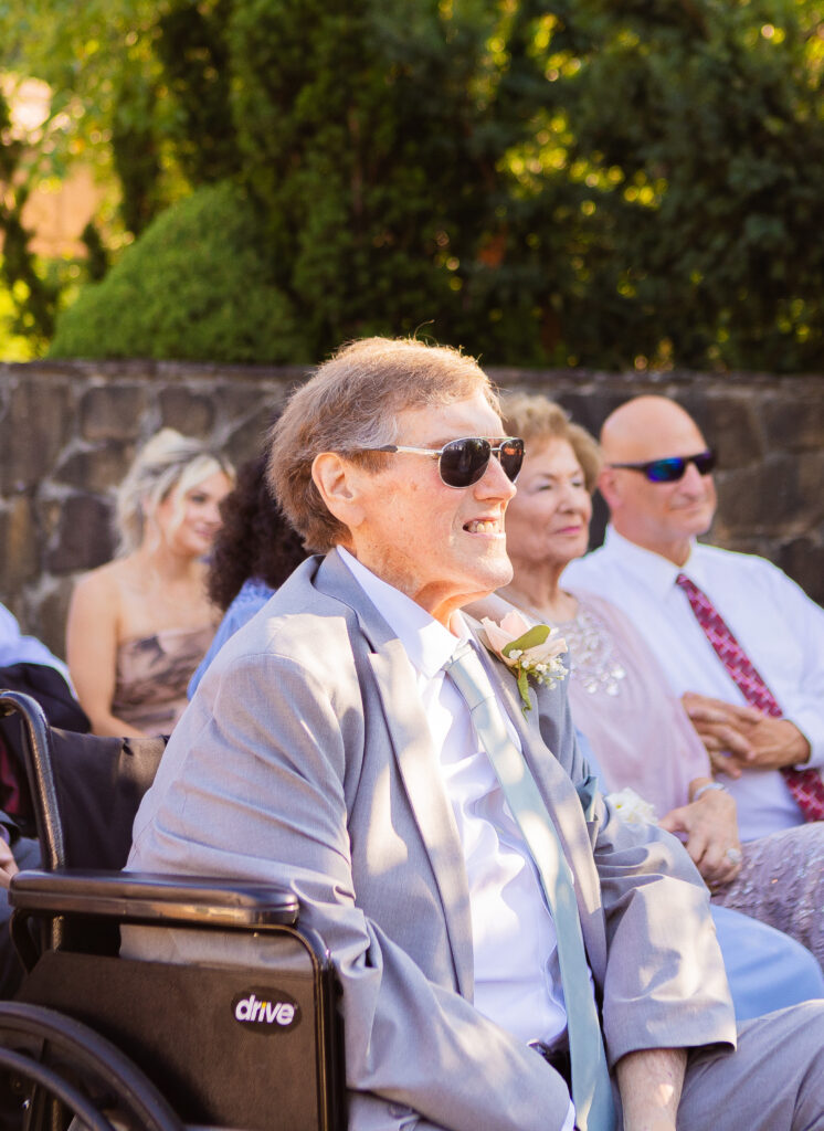 Father of the groom smiling at the bride and groom during a wedding ceremony.