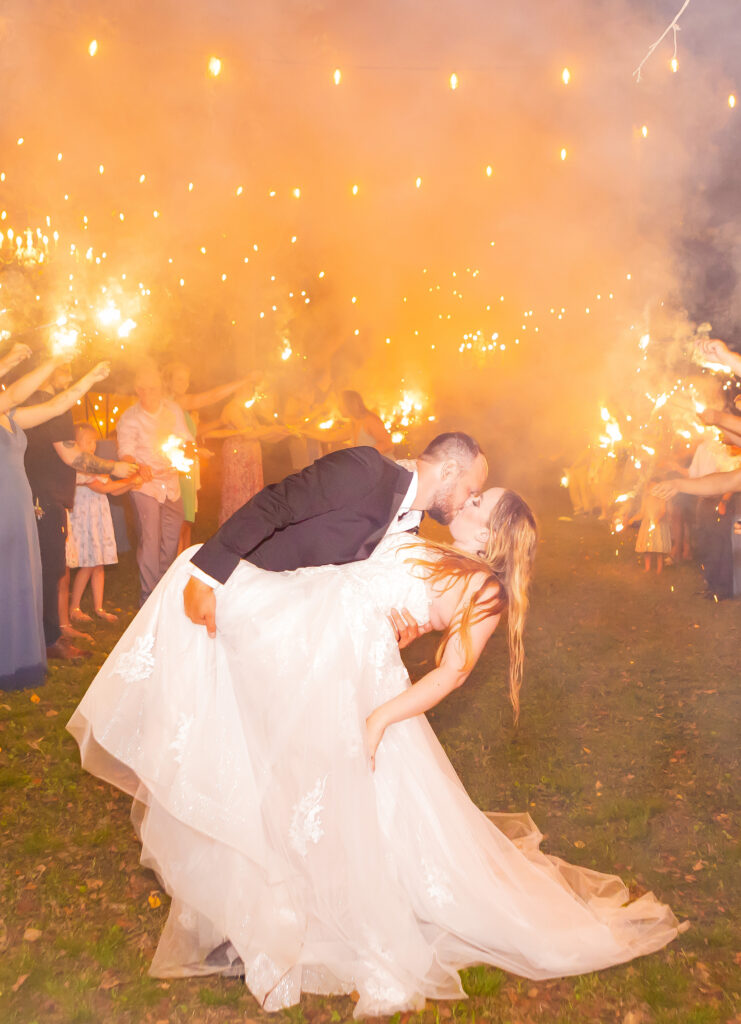 Groom dips his bride at the end of their sparkler exit at their waterfront wedding venue, Stone Garden in Westmoreland, NH.