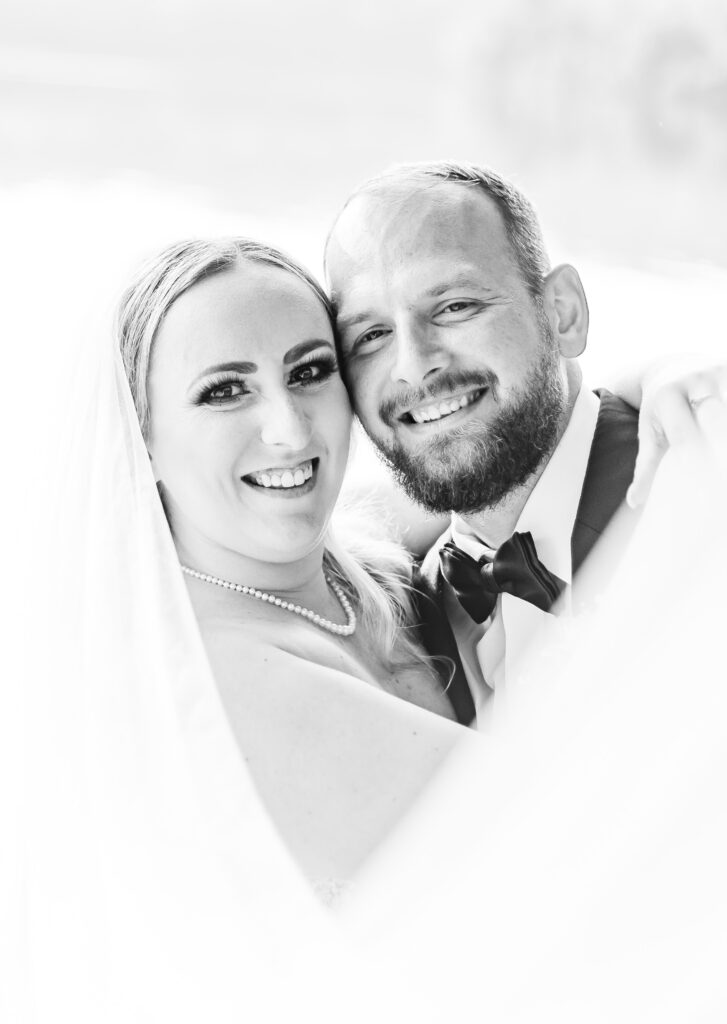 Bride and groom snuggle in the veil of the bride's wedding dress.