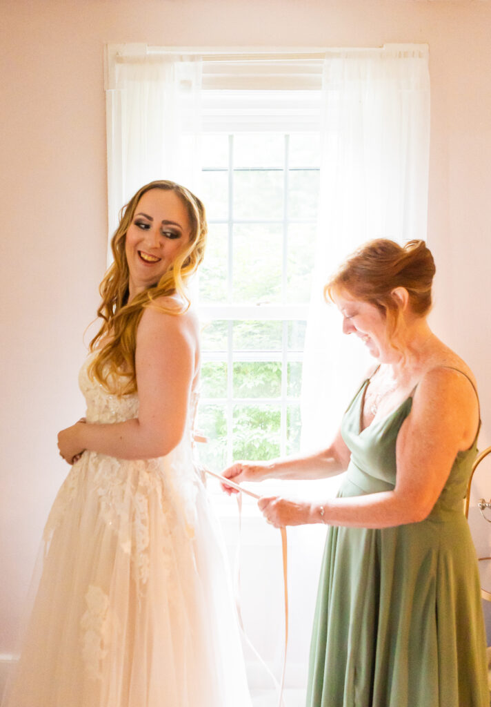 Mother of the bride is tying the brides dress at her garden wedding in NH.