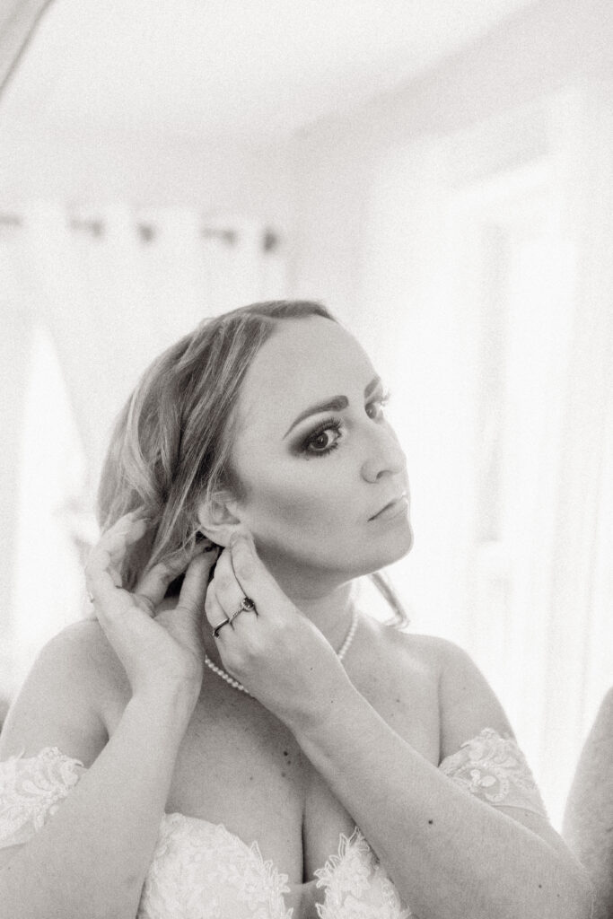 Bride is putting her earrings on in the mirror moments before her NH wedding ceremony in a garden.