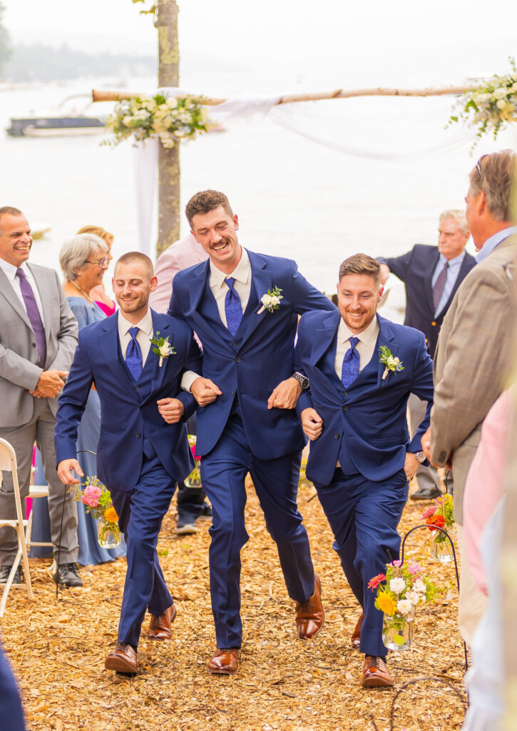 Three groomsmen walking arms linked back up the wedding aisle.