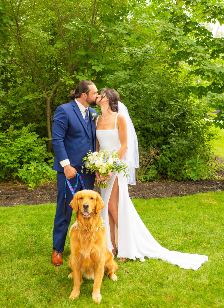 Bride and groom share a kiss while holding their golden retriever at their Lake Winnipesaukee Wedding.