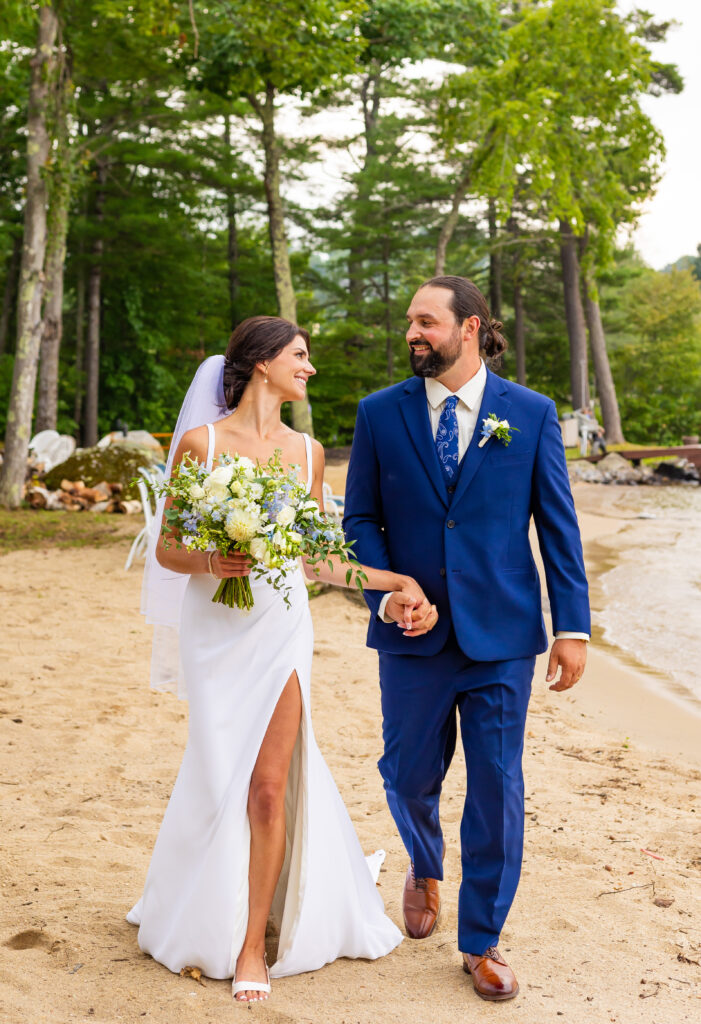 Bride and groom walking hand in hand on front of Lake Winnipesaukee.