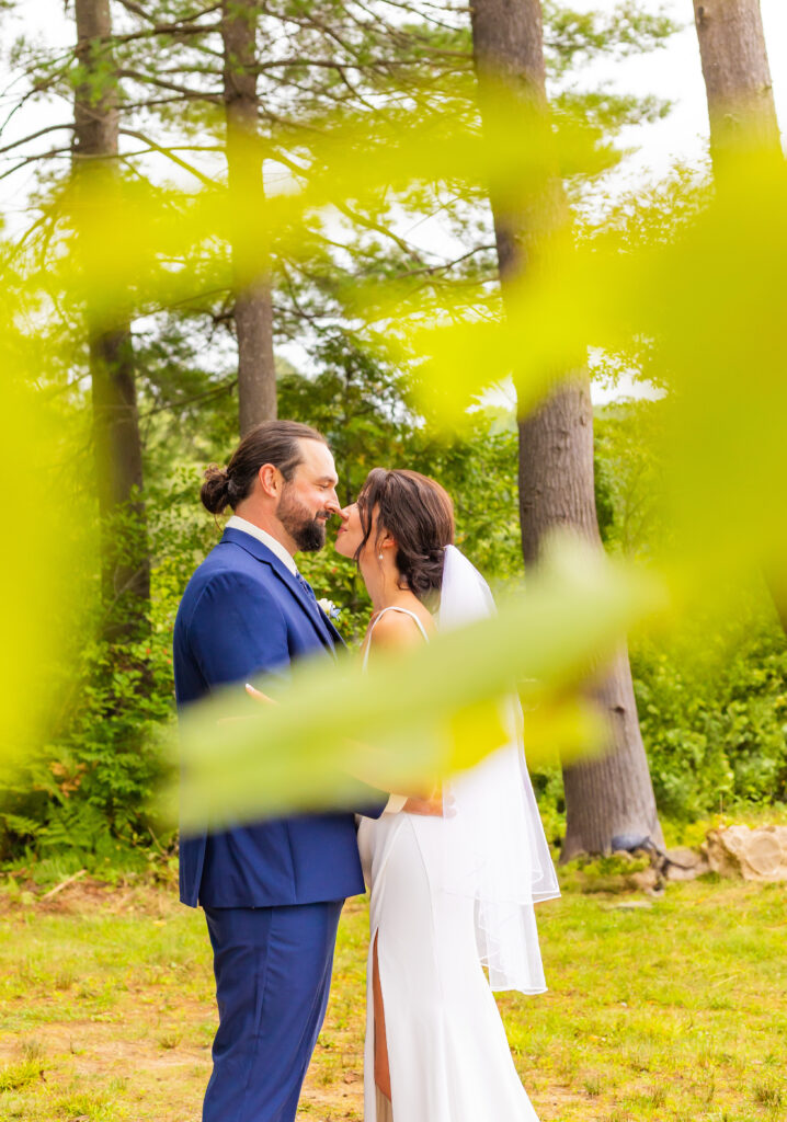 Bride and groom nuzzle noses through the branches.