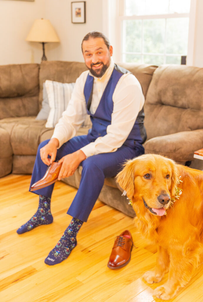 The grooms dog jumps in for a photo while putting his shoes on at a Mills Falls at the Lake wedding.