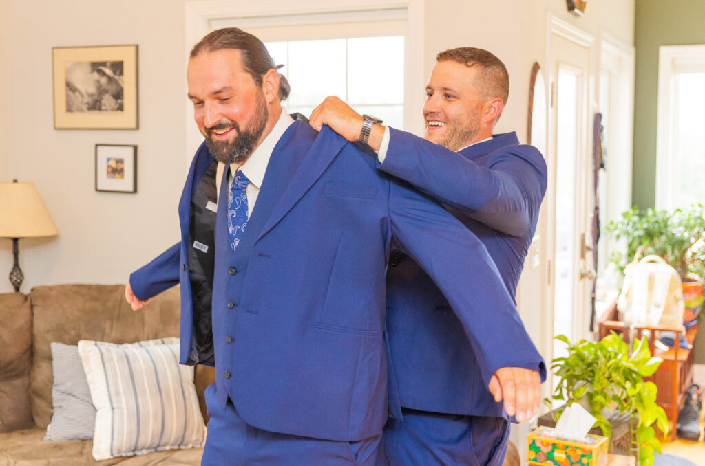 Groomsmen helps the groom put his suit jacket on.