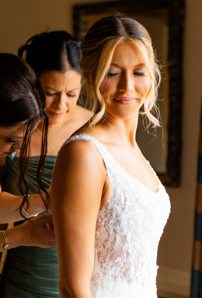 sister and mom helping the bride put her dress on at her wedding at the wolfeboro inn