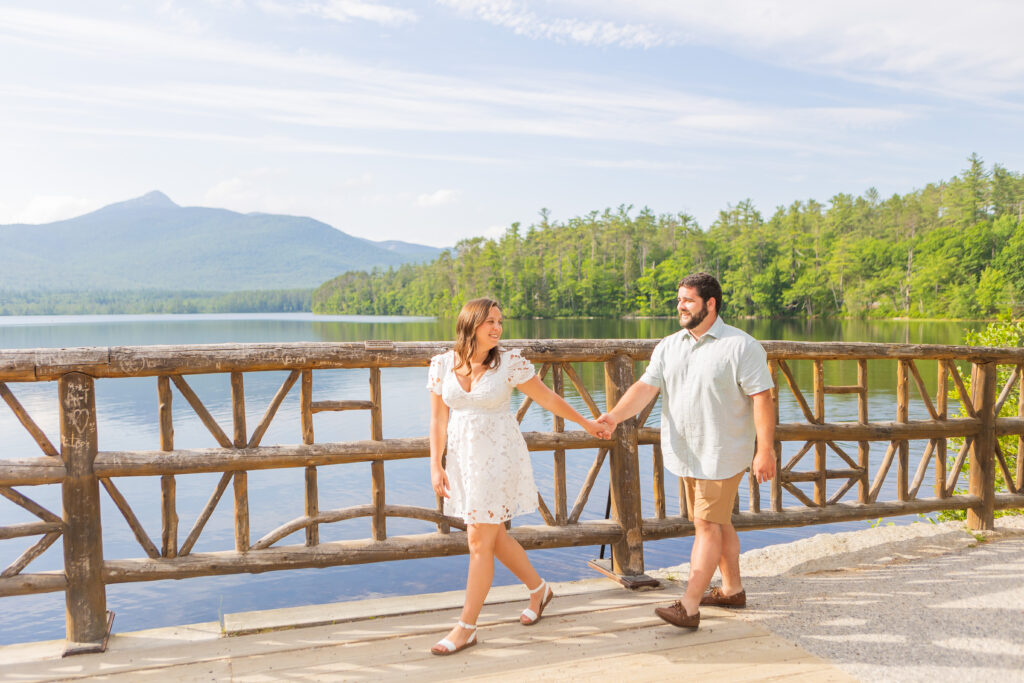 A couple walking along the water at their engagement session at Chocorua Lake in Tamworth, New Hampshire.